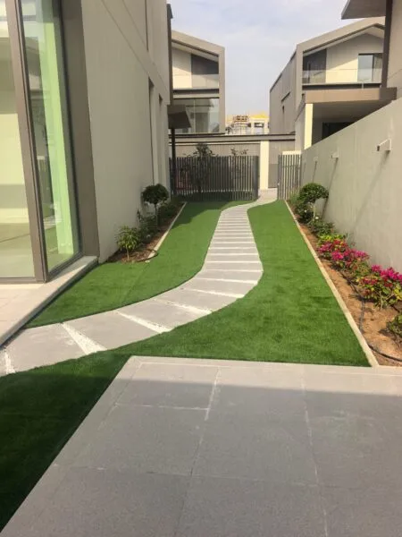 Modern villa landscaping in Dubai with artificial grass, curved stone pathway, plants, and boundary wall garden design