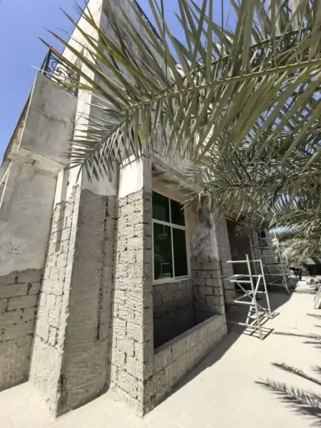 Partially renovated building exterior with exposed walls and palm leaves in the foreground.