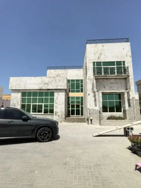 Modern house exterior with large glass windows, balcony, and a driveway with a black SUV parked in front.