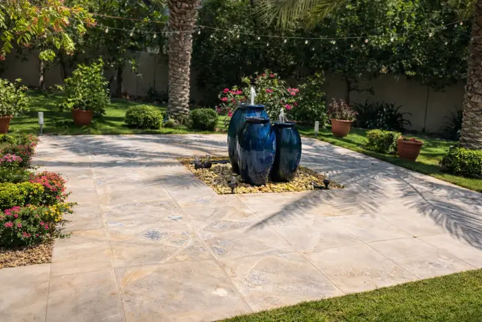 Beautiful landscaped garden patio with decorative blue water fountain, tiled flooring, and lush greenery