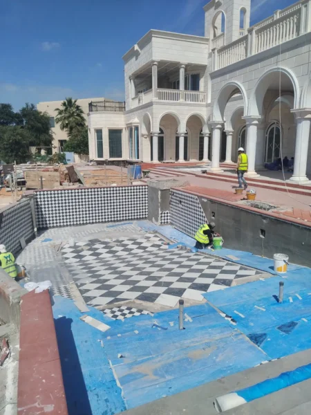 Workers tiling a swimming pool with black and white patterned tiles at a luxury villa construction site