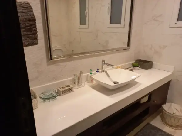 Modern bathroom vanity with white countertop sink, large mirror, and marble-style wall tiles