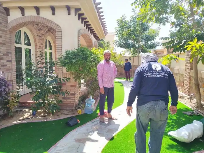 Flowers Yard team laying artificial grass rolls alongside a stone pathway at a Jumeirah villa in Dubai