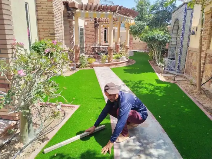 Grass · finishing Team finishing artificial grass edges along a curved stone pathway in a Jumeirah Dubai villa garden