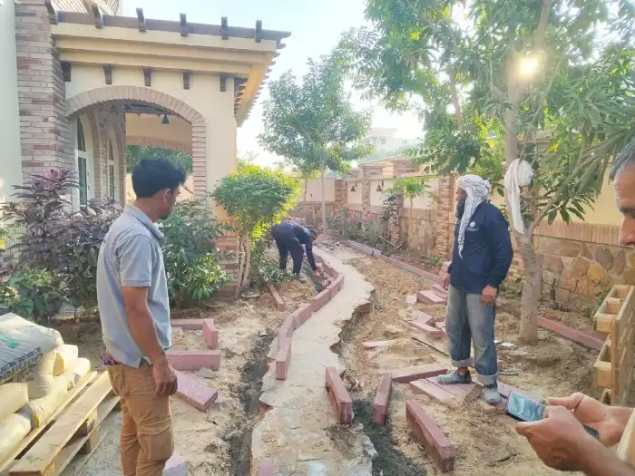 Landscaping team hand-laying brick edging for a curved garden path border in a Dubai villa landscaping project