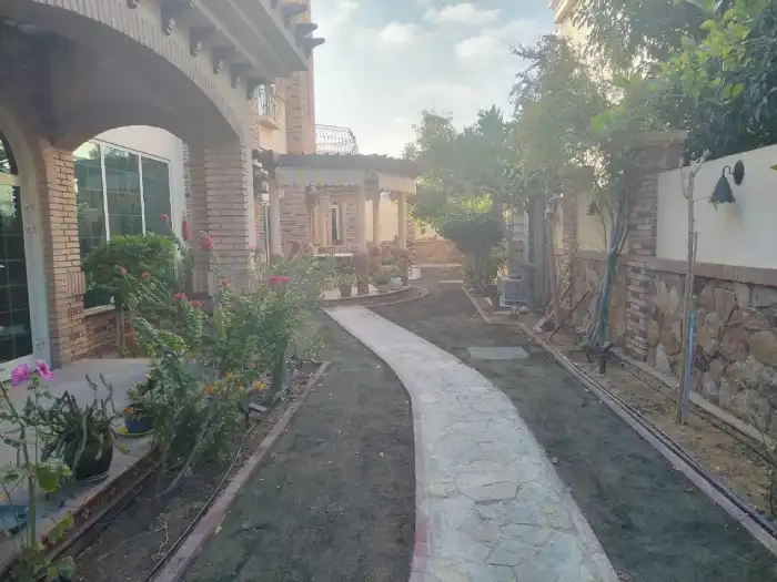 Long curved stone garden path at a Jumeirah villa with brick edging, planted borders, and pergola view
