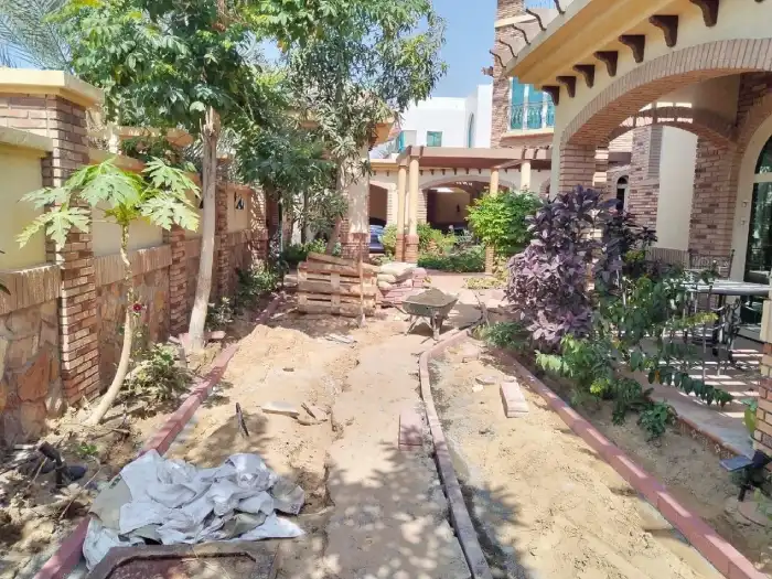 Bare sandy garden entrance at Jumeirah villa before landscaping, brick archway and existing plants