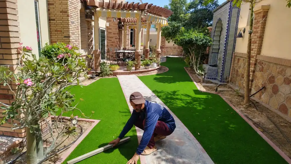 Worker installing artificial grass in a villa garden with paved walkway, outdoor patio, and professional landscaping service setup