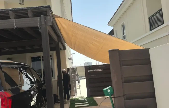 Beige shade sail installed beside a wooden carport at a luxury villa driveway in Dubai.