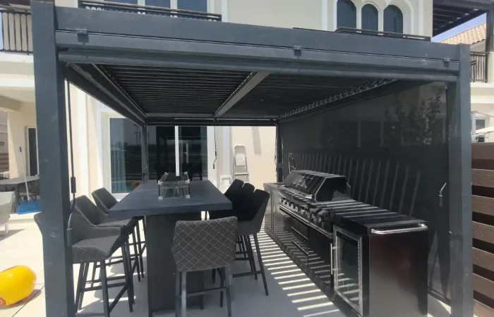 Black aluminium pergola with outdoor kitchen, barbecue, bar table, and seating at a luxury villa in Dubai.