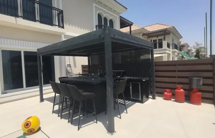 Poolside black aluminium pergola with outdoor kitchen, bar seating, and louvered roof at a luxury Dubai villa.