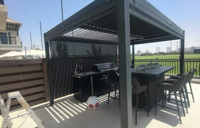 Modern black aluminium pergola with a louvered roof, outdoor barbecue, bar table, and seating at a Dubai villa.